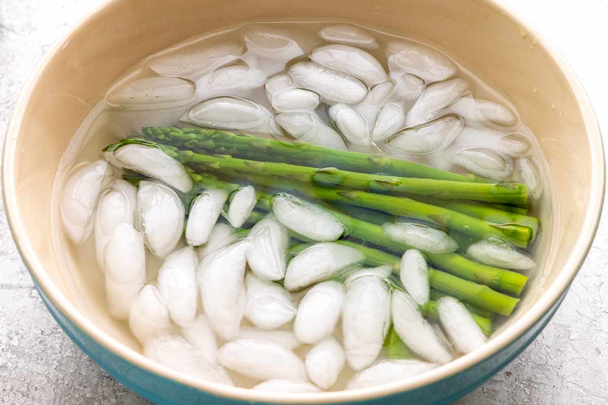 Asparagus spears placed in a large bowl of ice water.