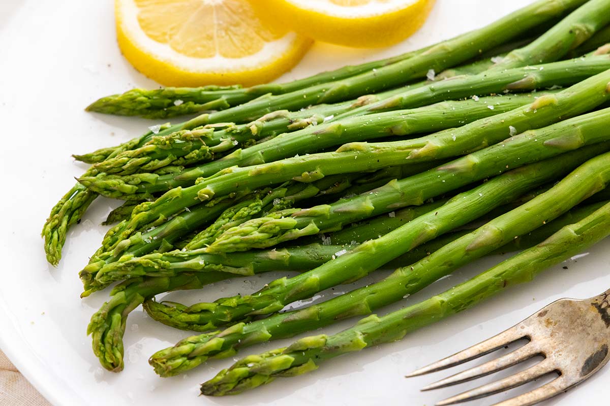 Plate of seasoned asparagus, lemon slices, and a metal fork.