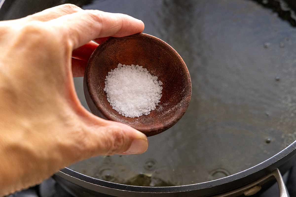 Person about to pour salt into a pot of water.
