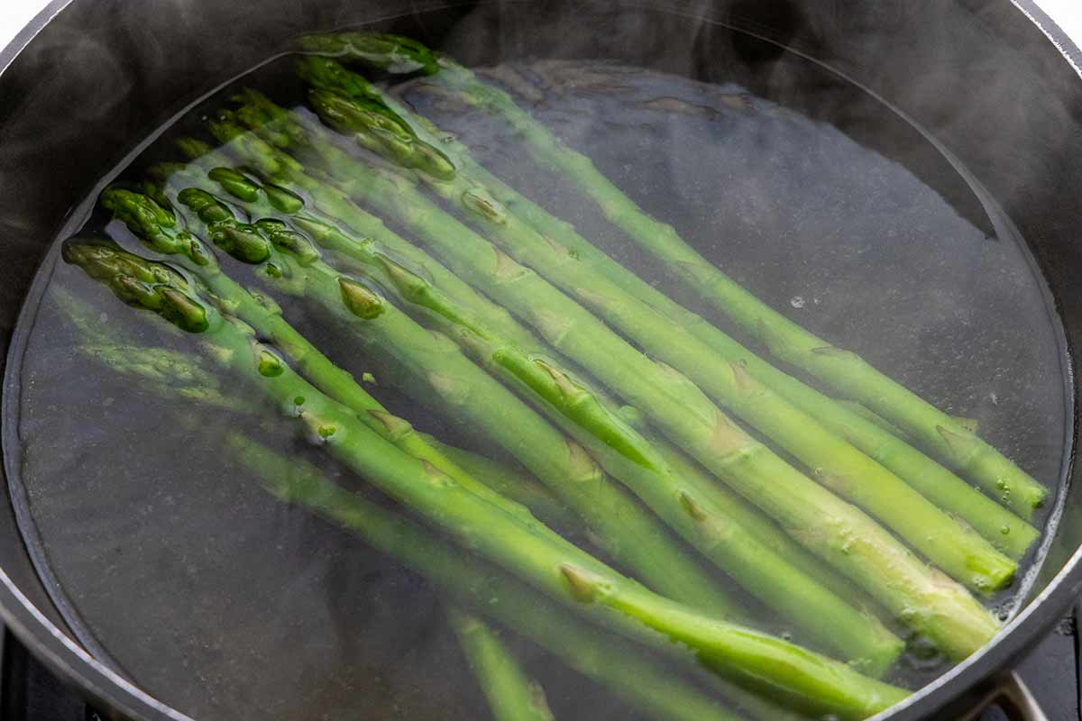 Several asparagus spears submerged in a pot of boiling water.