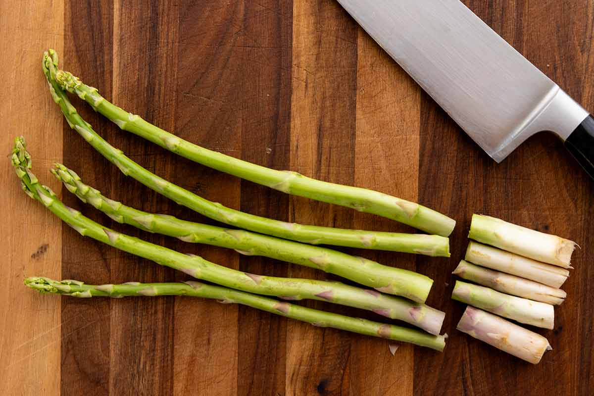 Asparagus spears sliced into pieces on a wooden cutting board.