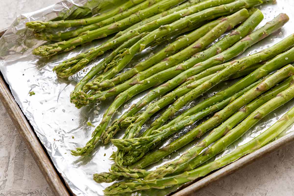 Seasoned asparagus spears on a foiled lined sheet pan.