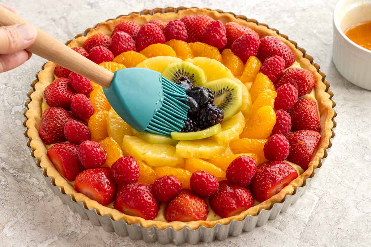 Brush mopping the top of a fruit tart with apricot jam.