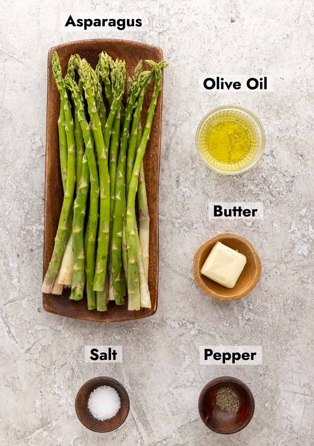 Asparagus bunch on a plate next to bowls of olive oil, butter, salt, and pepper.