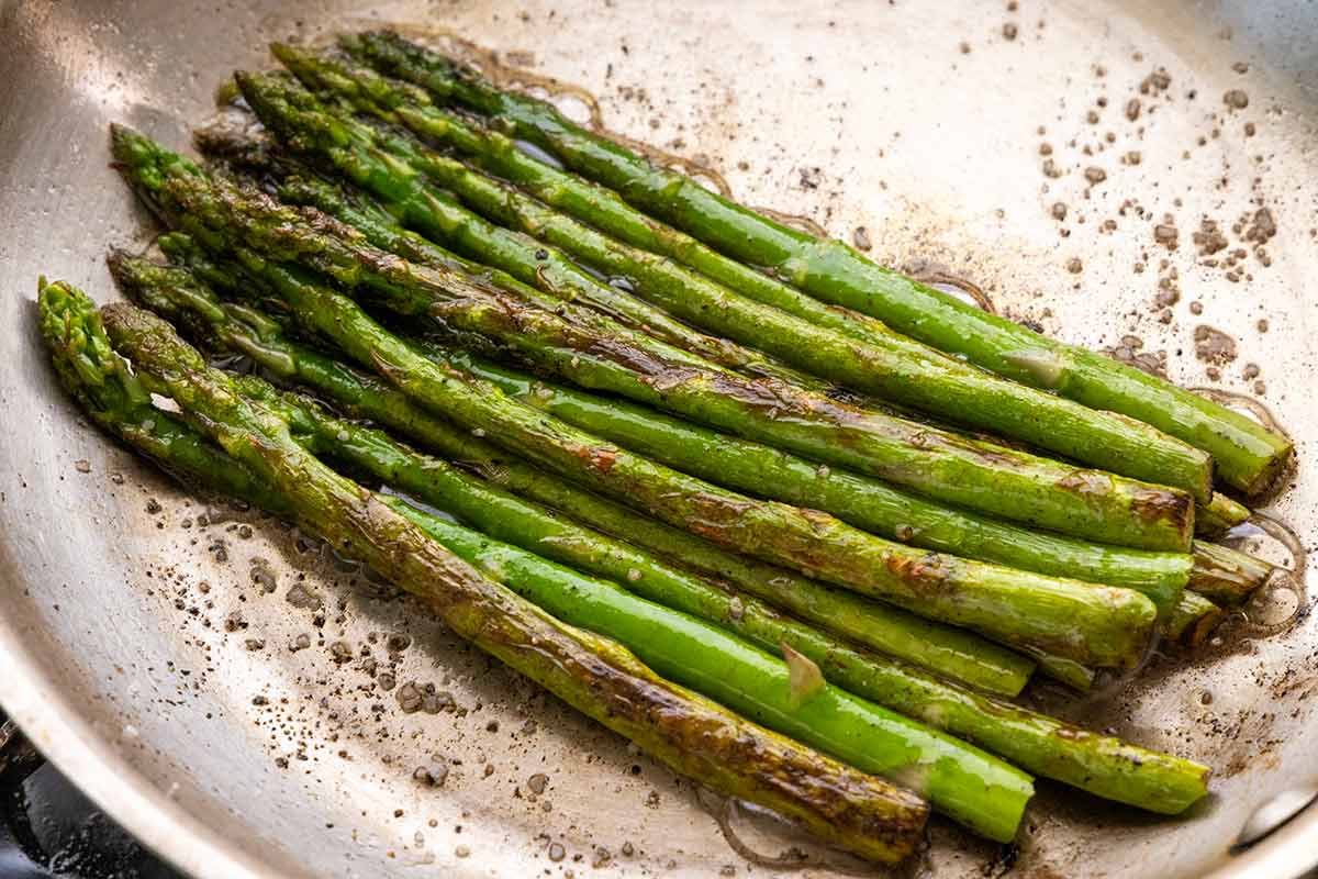 Asparagus being cooked in a stainless pan.