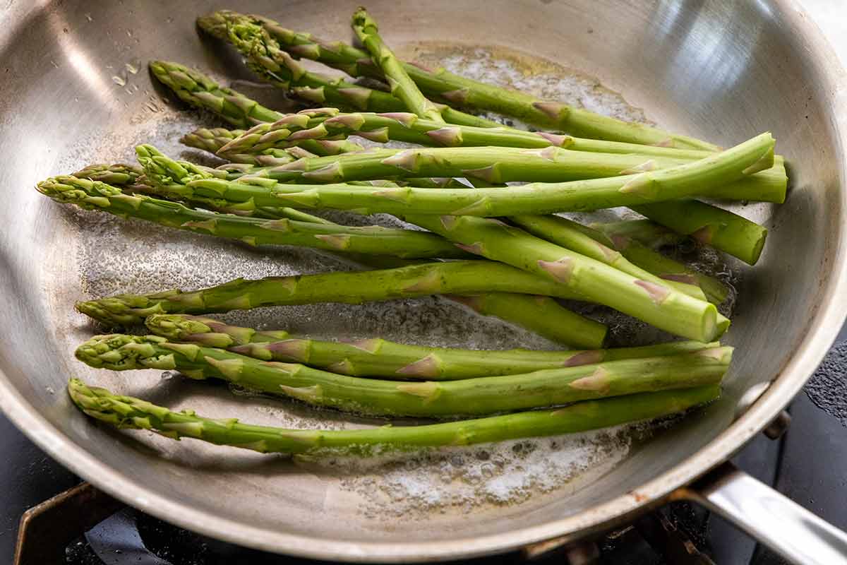 Asparagus spears placed in a pan with bubbling melted butter.