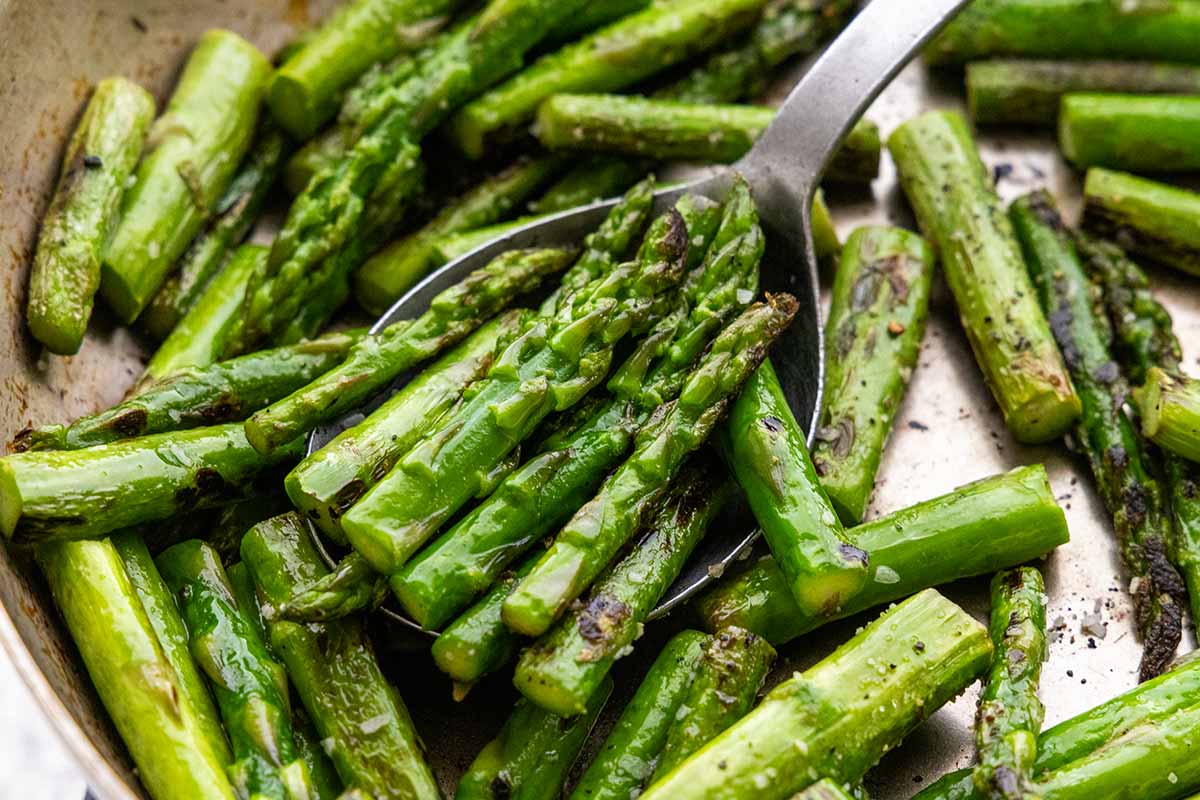 Asparagus pieces sauteing in a metal pan.