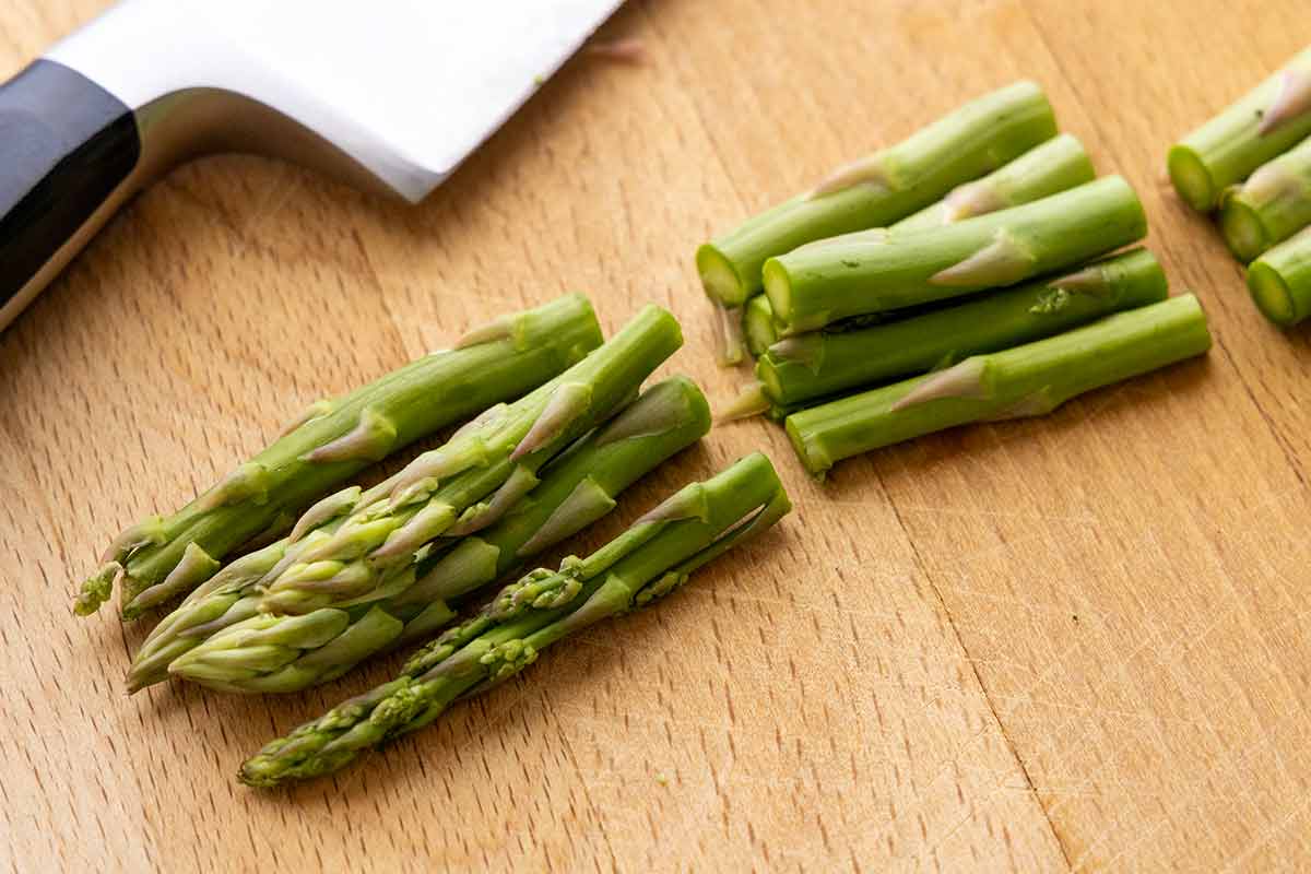 Asparagus spears on a wooden cutting board sliced into smaller pieces.