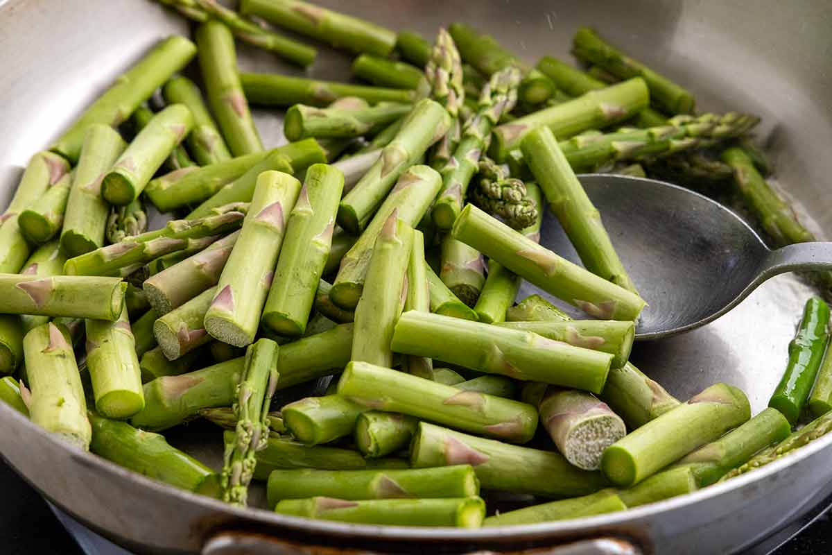 Raw asparagus pieces placed in a large stainless steel pan.