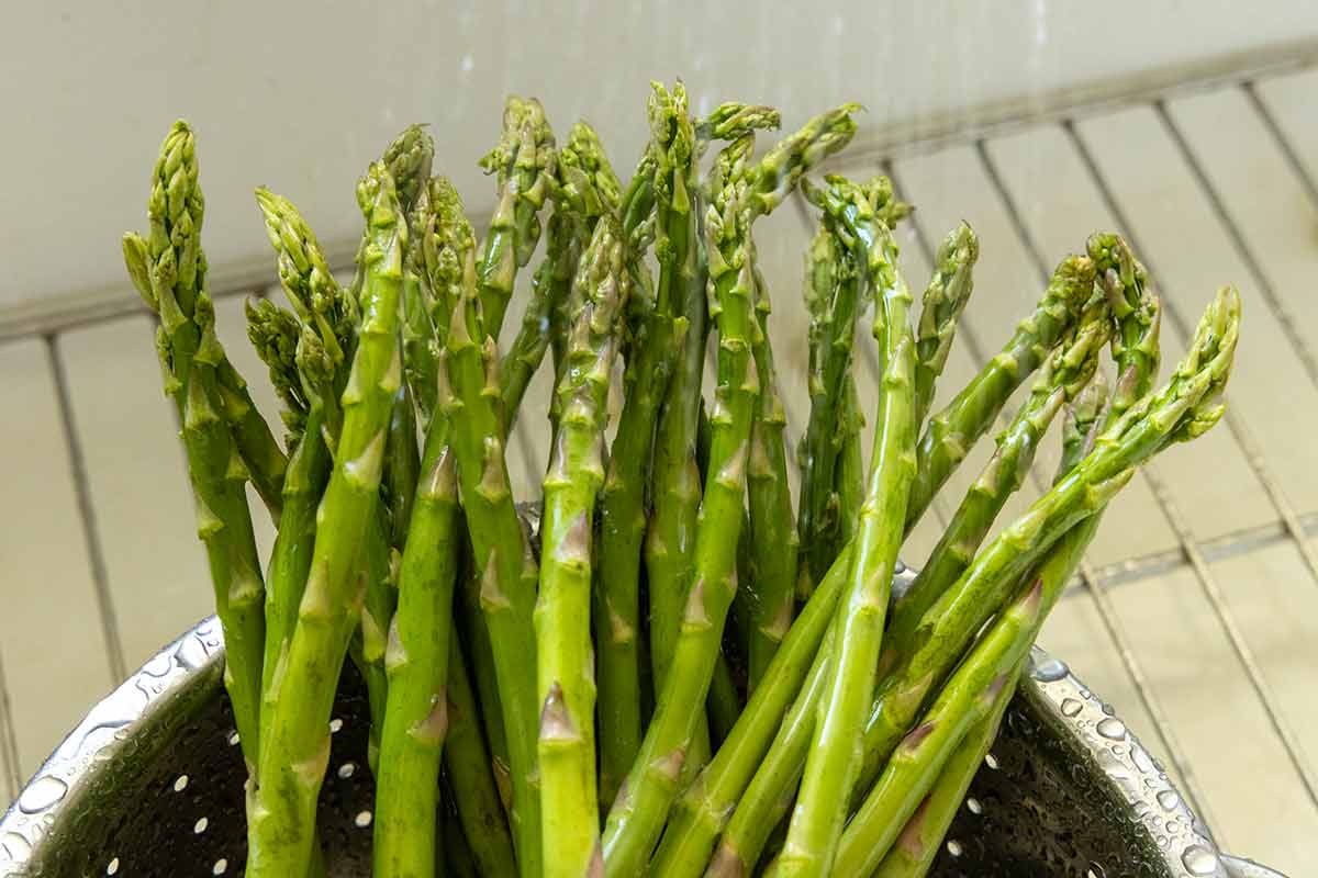 Asparagus in the sink being rinsed with water.
