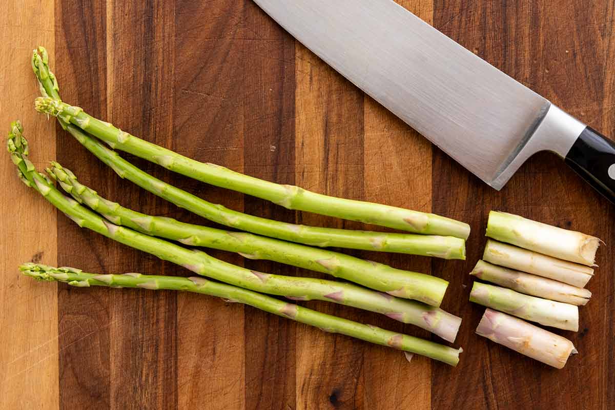 Asparagus spears on a wooden cutting board with the ends cut off.