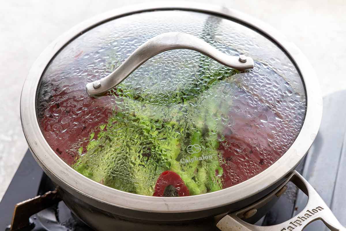 Saucepan with a clear glass lid showing asparagus being steamed.
