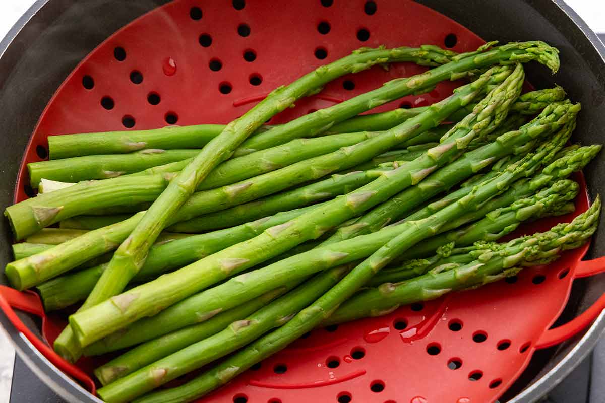 Asparagus spears on a red steamer basket in a saucepan.