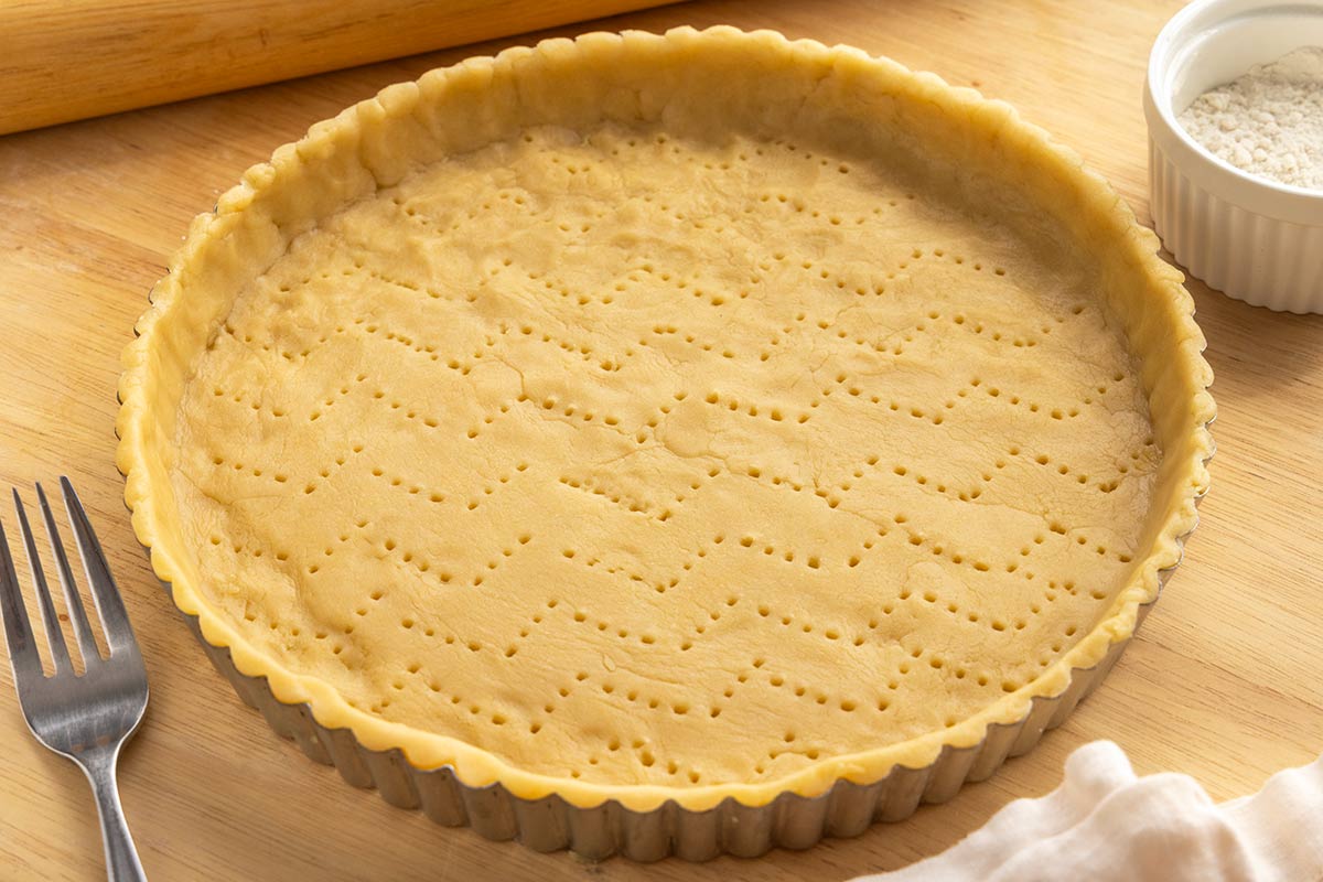 Metal fork next to a raw tart crust with holes poked into it.
