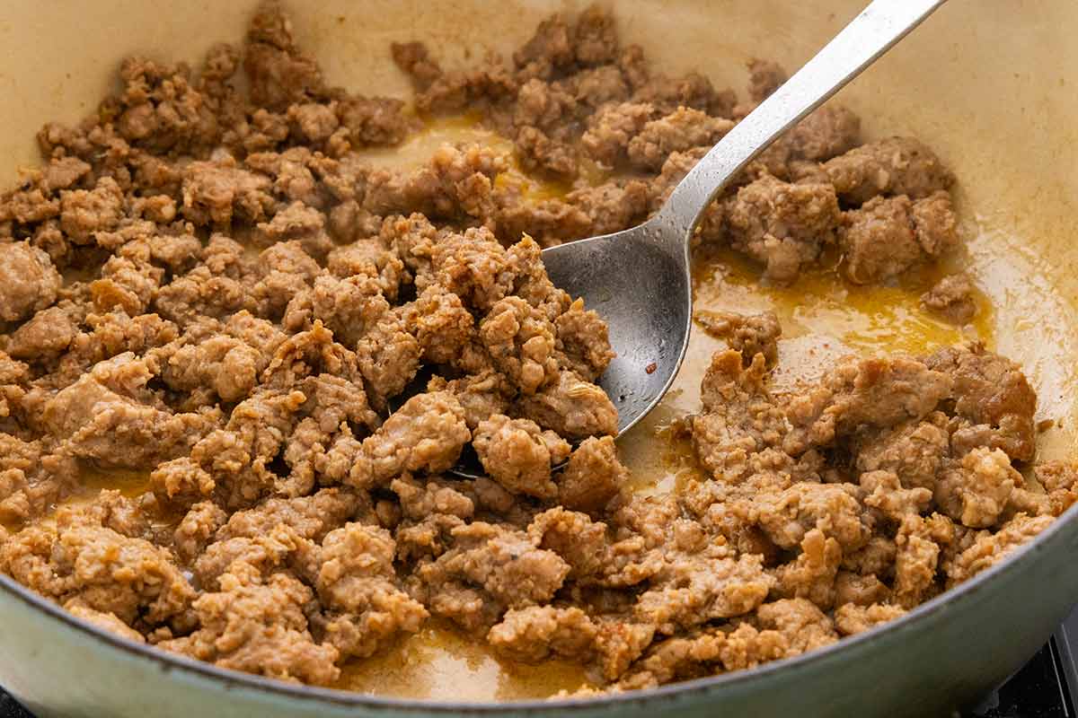 Ground Italian sausage browning in a pot and being broken into pieces with a metal spoon