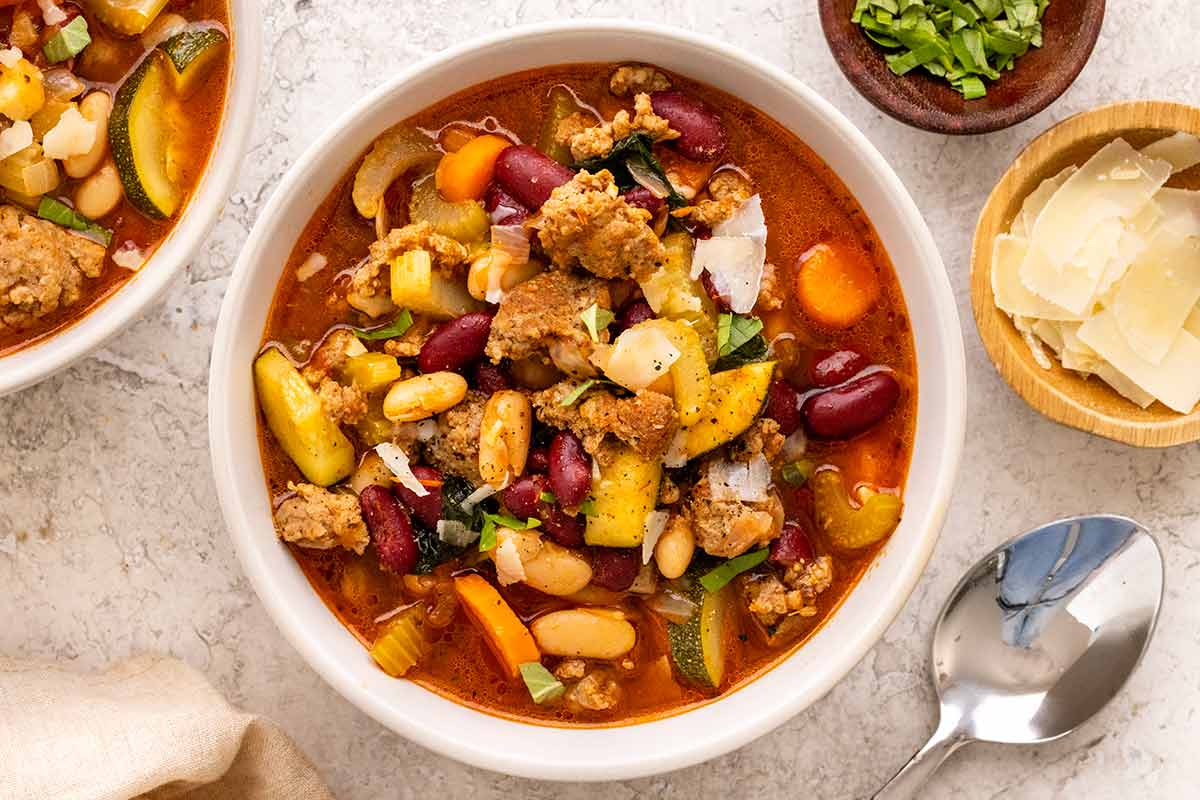 A bowl of Italian sausage soup with kidney beans, cannellini beans, zucchini, and carrots, topped with parmesan