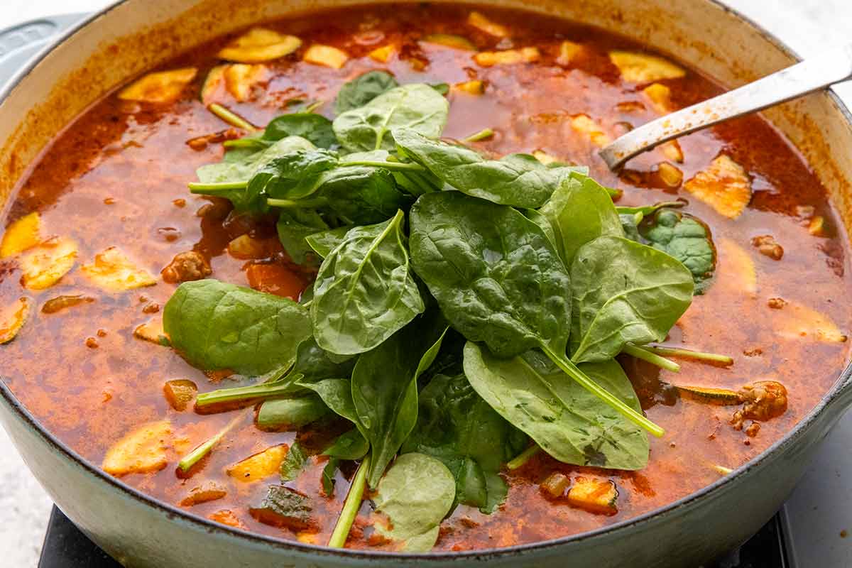 Adding a pile of fresh spinach to the pot of simmering Italian sausage soup