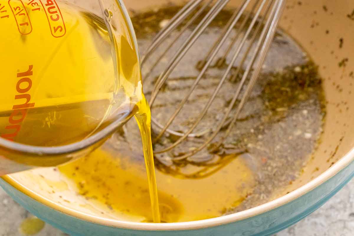 Olive oil being poured into a bowl with a whisk to make a salad dressing.