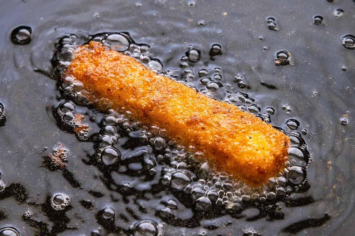 A single cheese stick frying in vegetable oil.