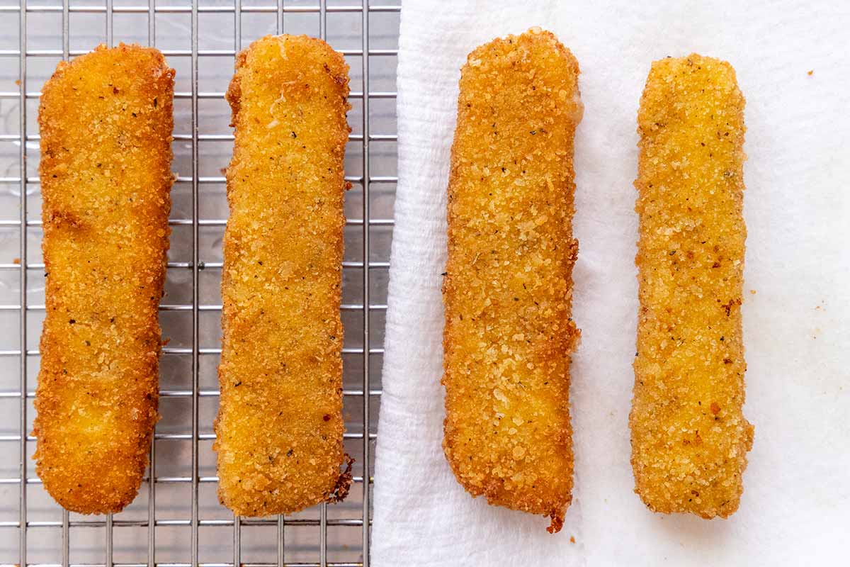 Crispy cheese sticks placed on a wire rack and also on a paper towel.