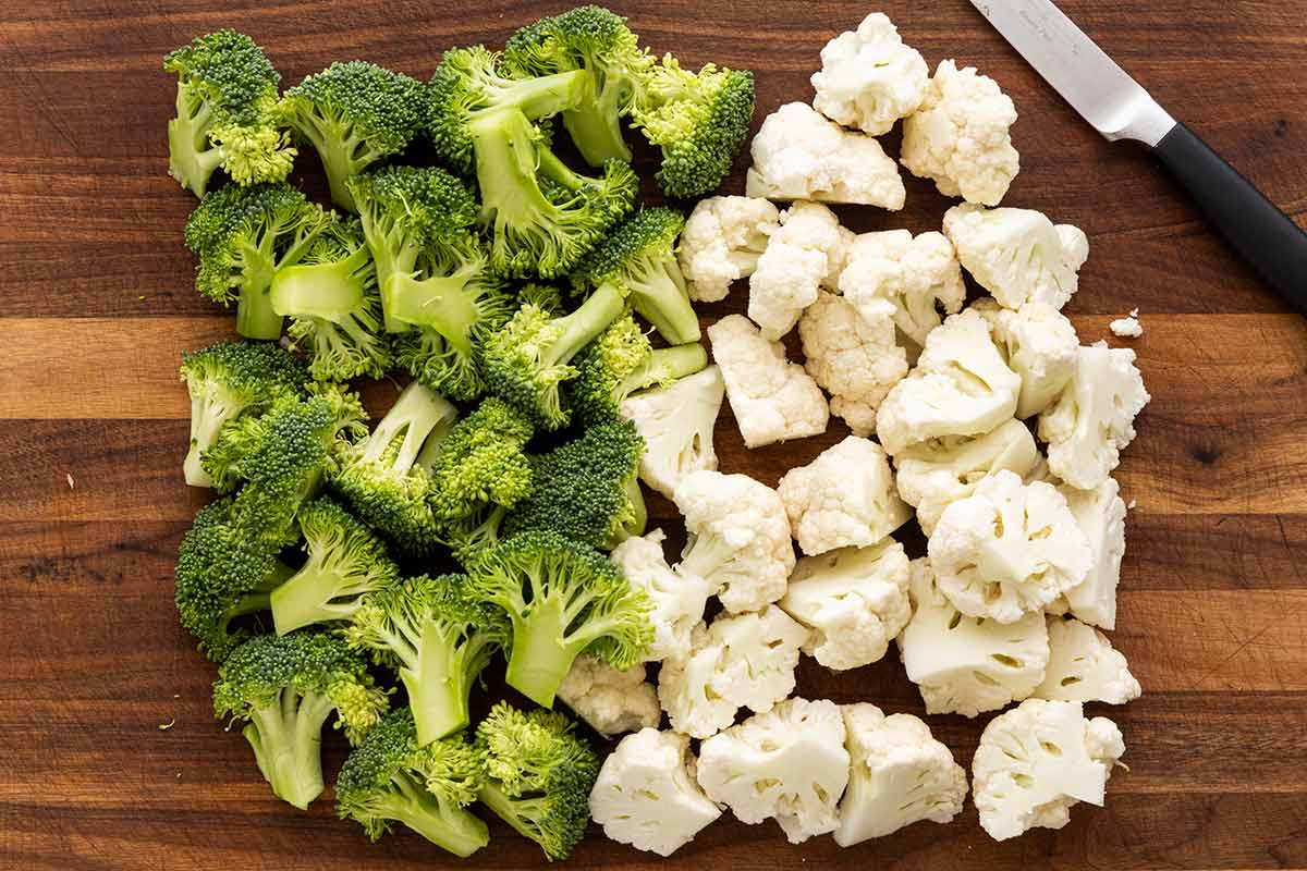 Broccoli and cauliflower florets cut into uniform pieces on a wooden cutting board