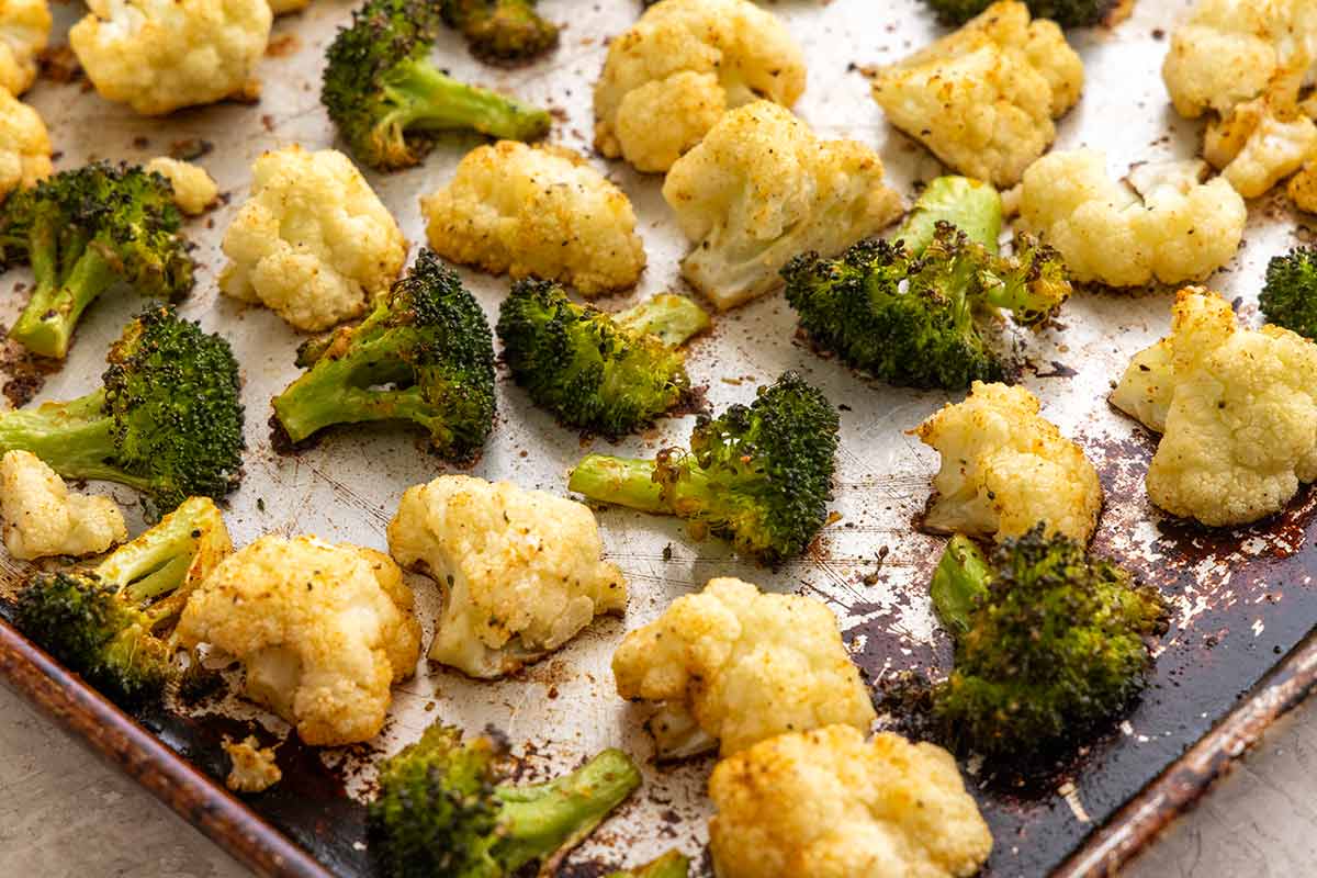 Broccoli and cauliflower florets seasoned and spread in a single layer on a metal baking sheet