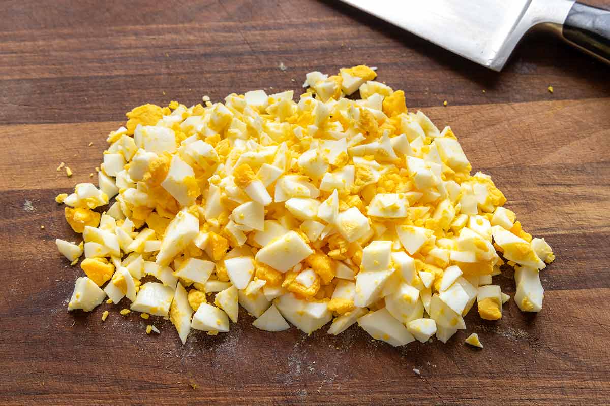 Chopped pieces of hard boiled eggs on a wooden cutting board.