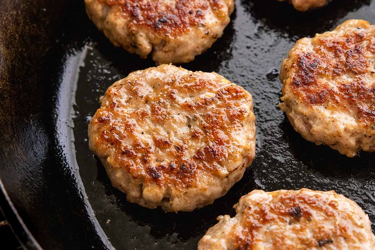 Golden brown breakfast sausage patties cooking in a cast-iron skillet