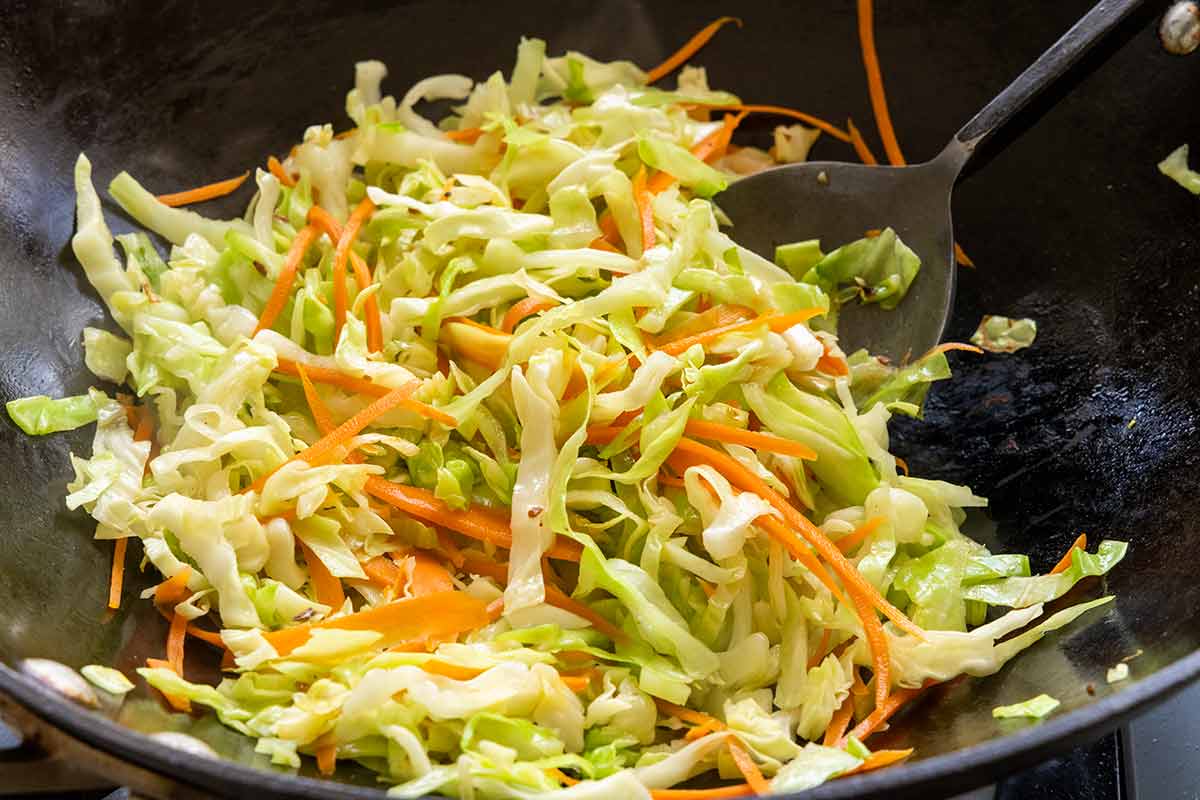 Green cabbage and shredded carrots stir frying in a pan.