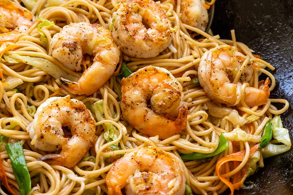 Shrimp placed over noodles and vegetables inside a pan.