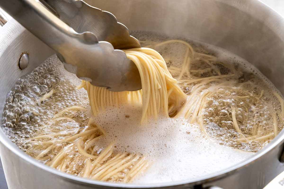 Lo mein noodles being cooking in a pot of water.