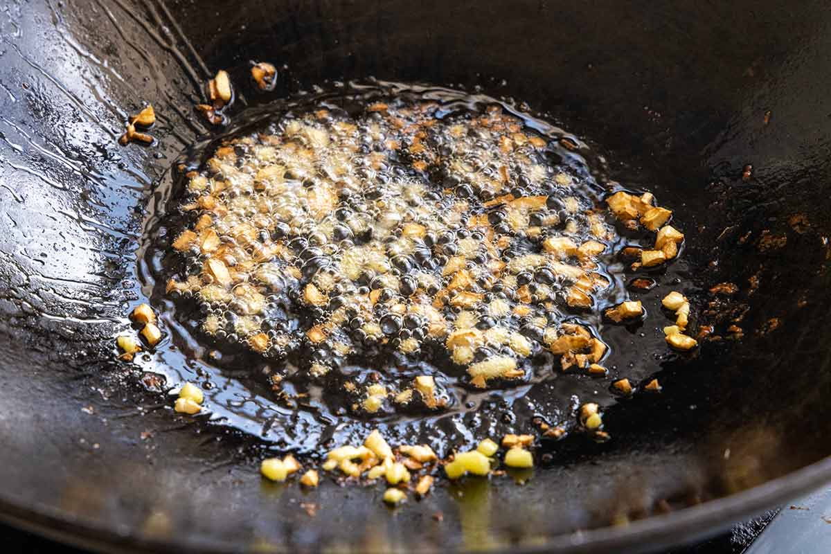 Pieces of garlic and ginger sauteing in a wok.