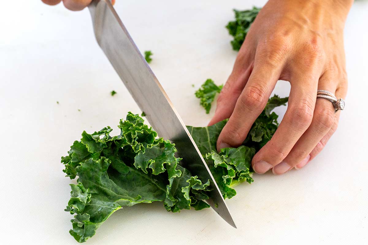 Cutting fresh curly kale leaves with a chef's knife on a cutting board.