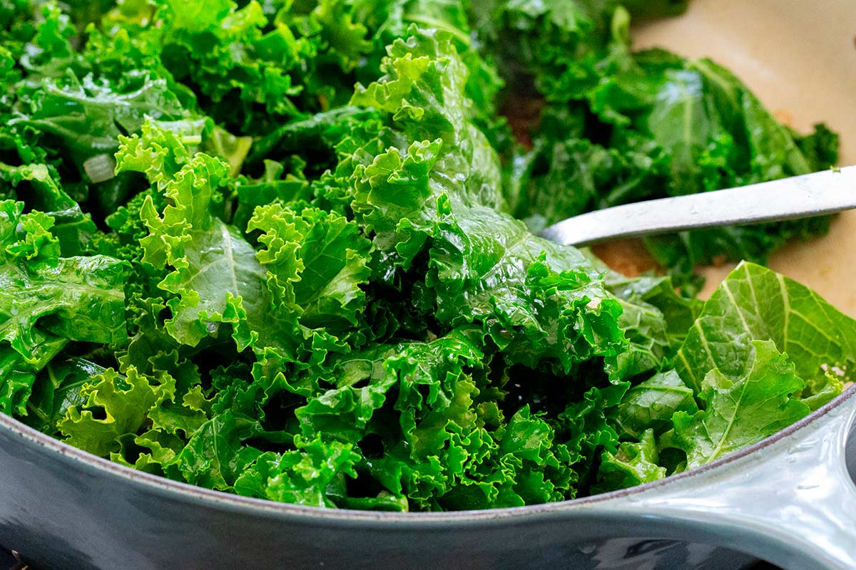 Chopped curly kale leaves added to a pan over sautéed onions and garlic.