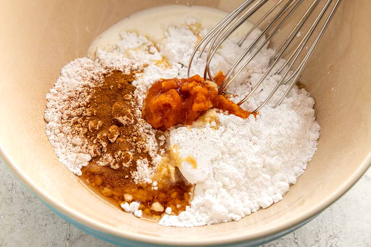 Powdered sugar, pumpkin puree, spices, and syrup in a mixing bowl with a wire whisk.