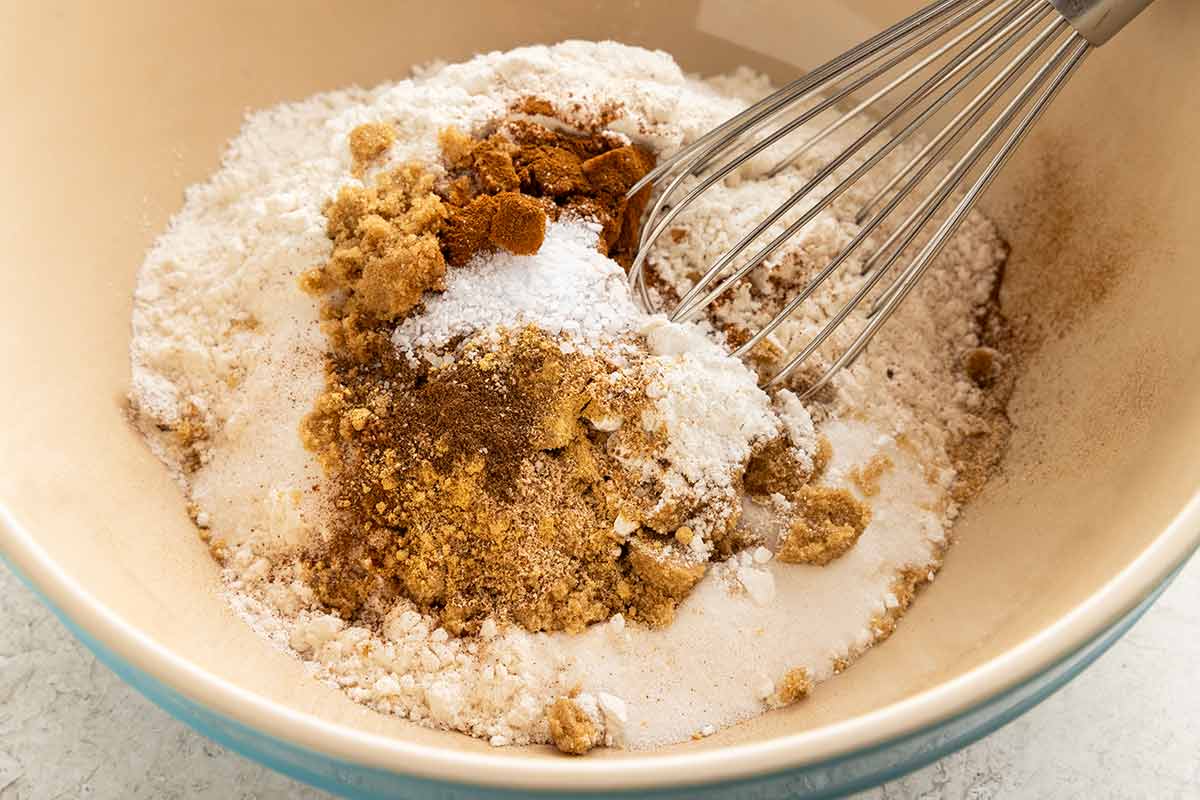 Flour, sugars, and ground spices in a mixing bowl with a wire whisk.