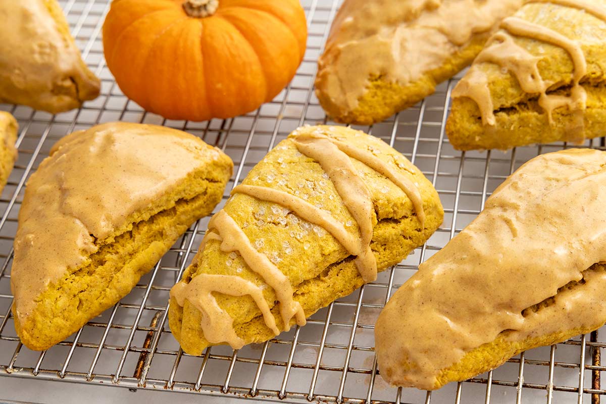 Baked pumpkin scones topped with smooth and drizzled maple glaze resting on a wire cooling rack.