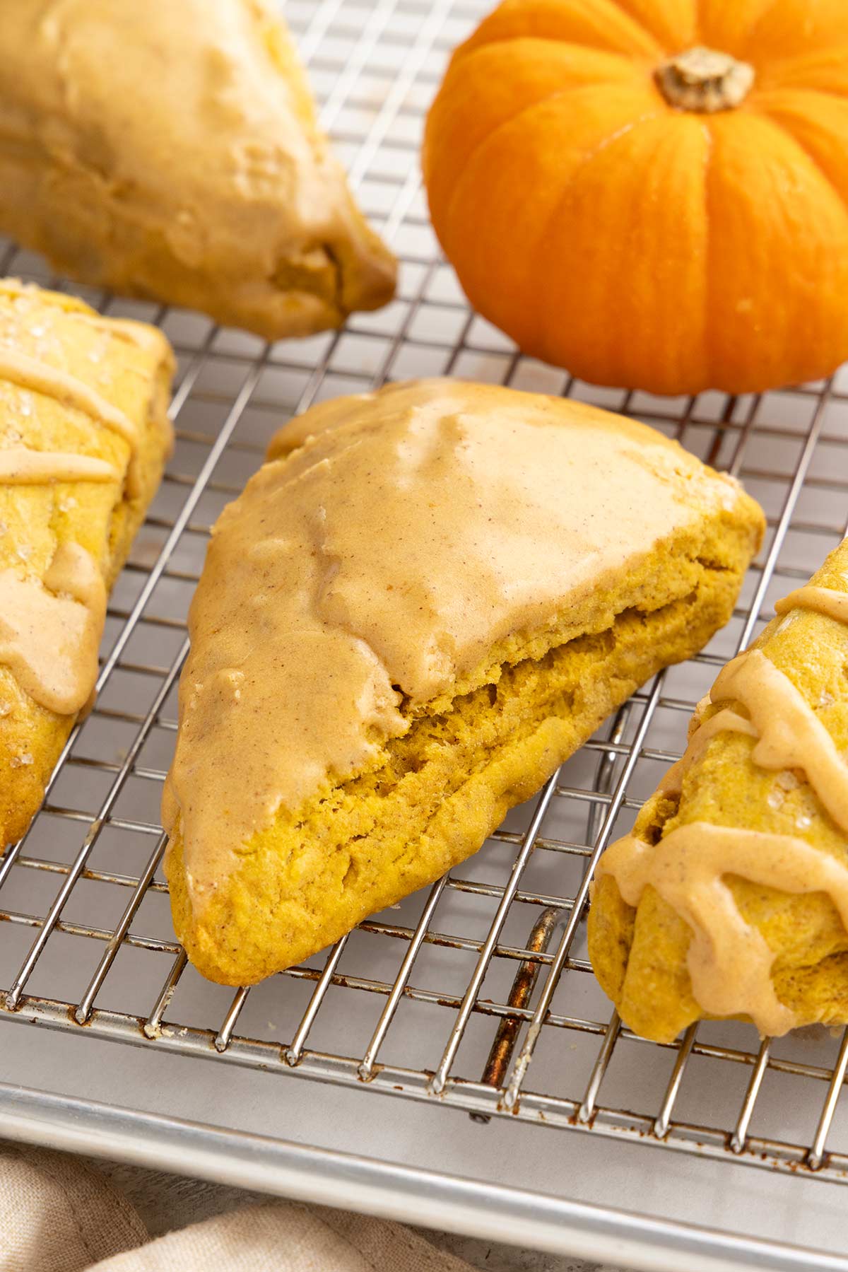 Glazed pumpkin scones resting on a wire cooling rack next to a small pumpkin.