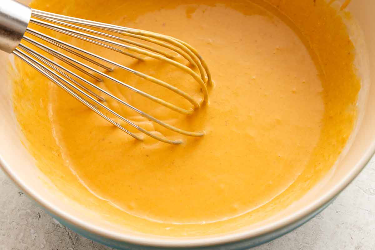 Whisked wet ingredients forming a smooth orange pumpkin mixture in a mixing bowl.