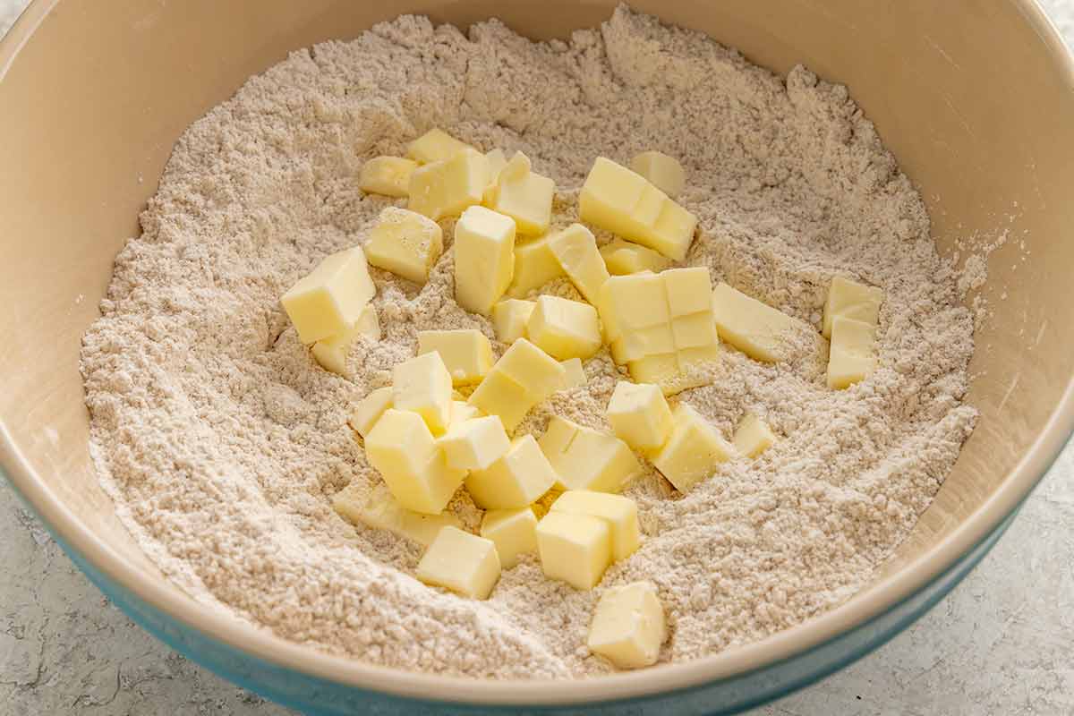Cubes of cold butter scattered over dry ingredients in a mixing bowl.