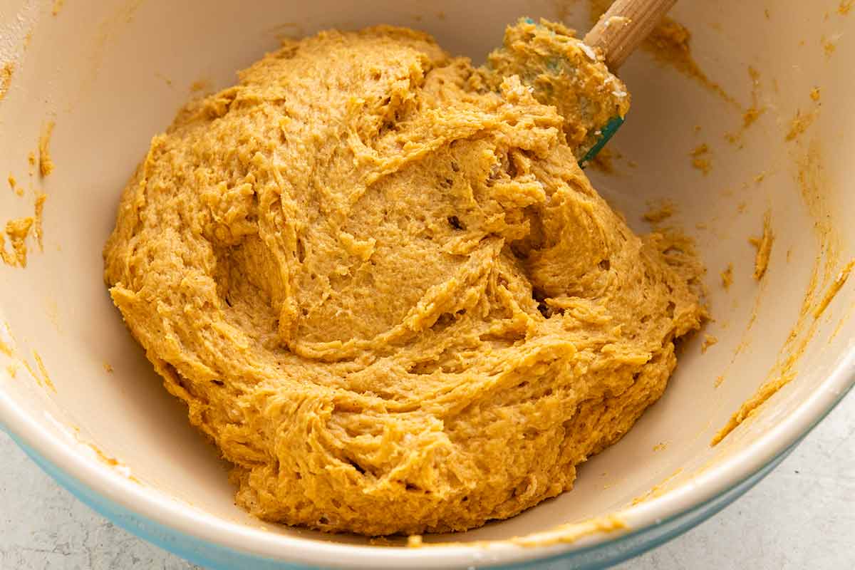 Thick, orange pumpkin scone dough mixed in a bowl with a spatula.
