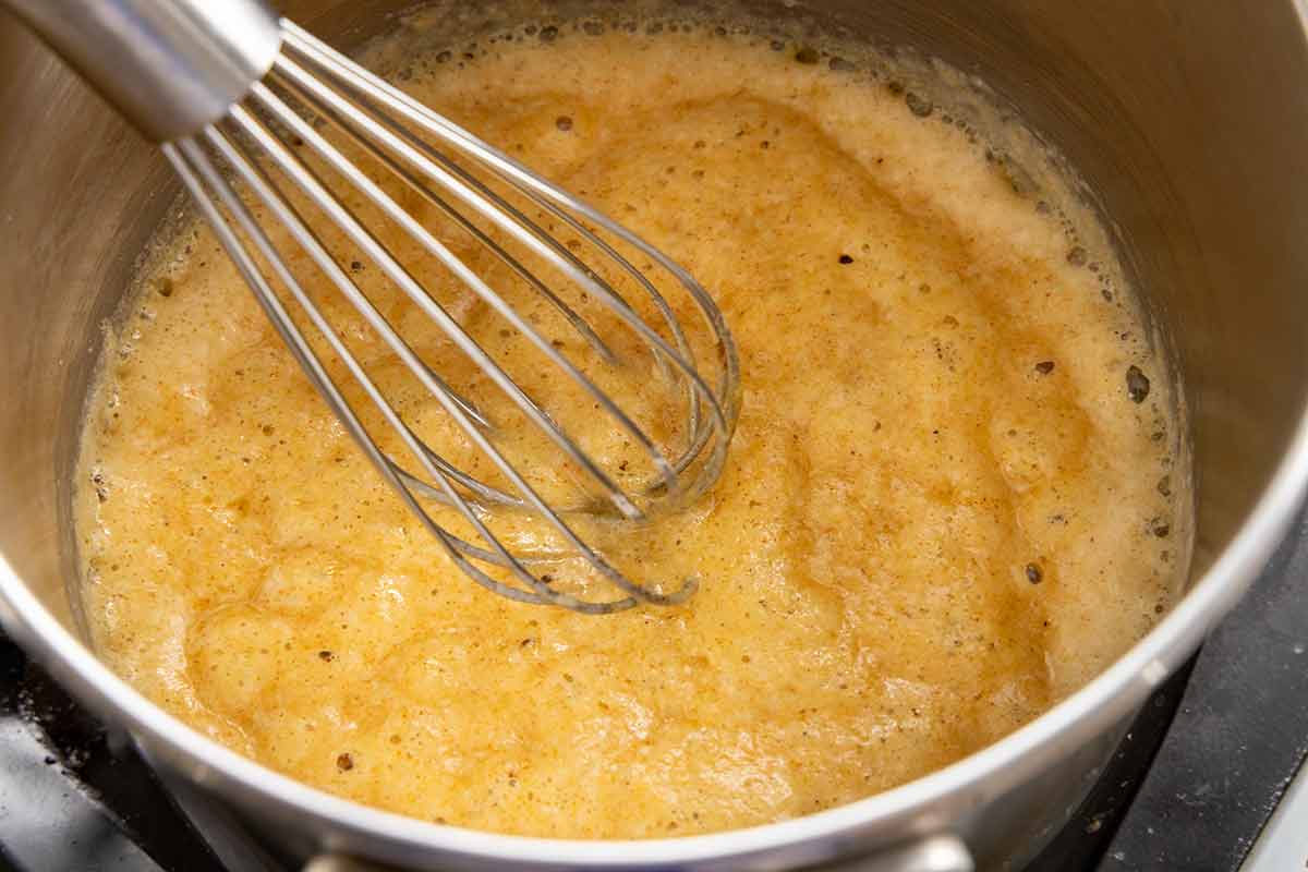 Whisking butter and flour in a saucepan until the roux turns a pale blonde color.