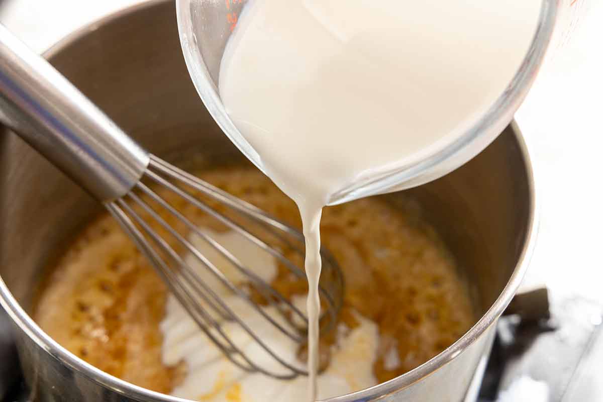 Milk being poured into a saucepan with spiced roux, whisked to form the beer cheese sauce base.