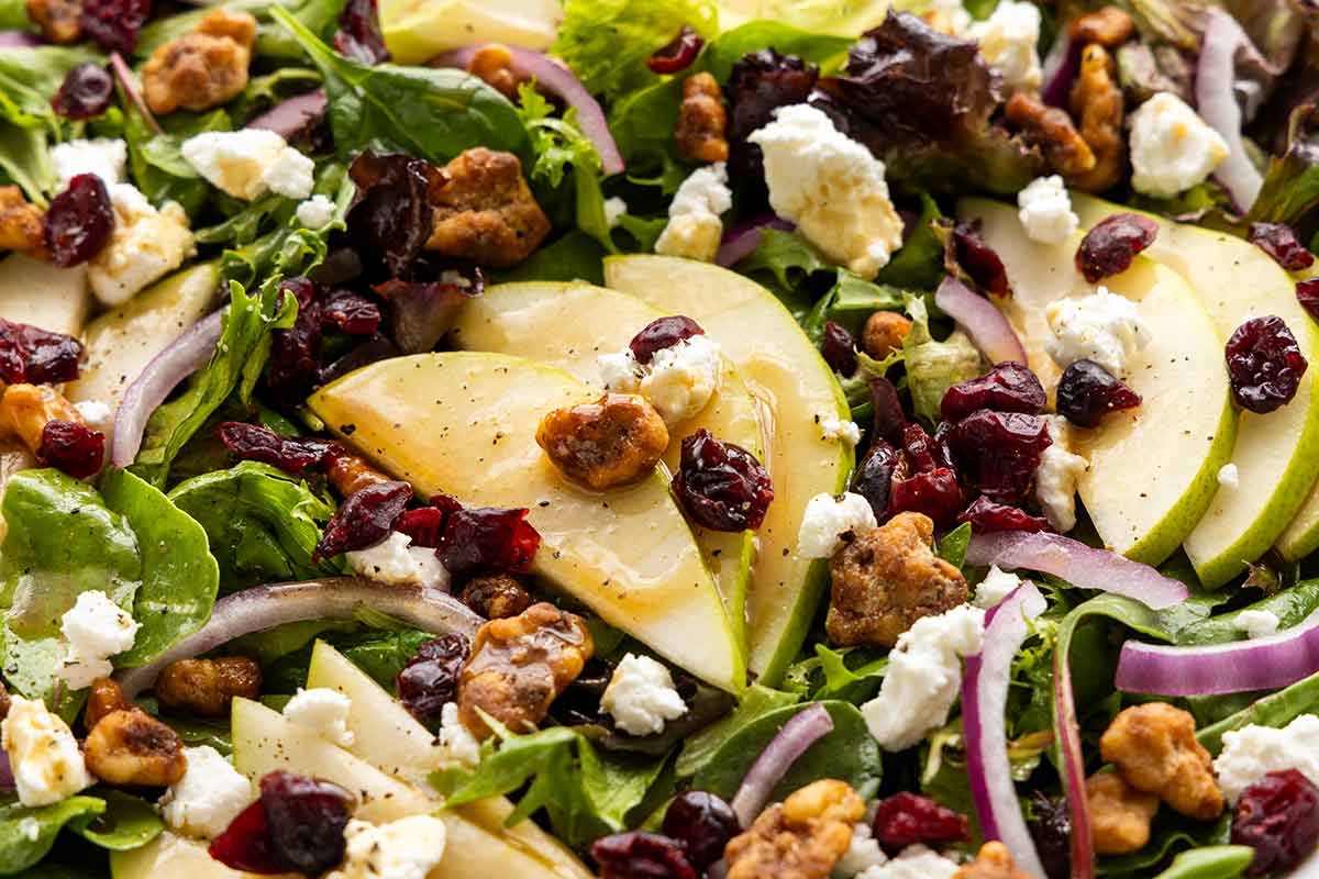 Assembled pear salad with fresh pear slices, goat cheese crumbles, dried cranberries, candied nuts, and sliced red onion.