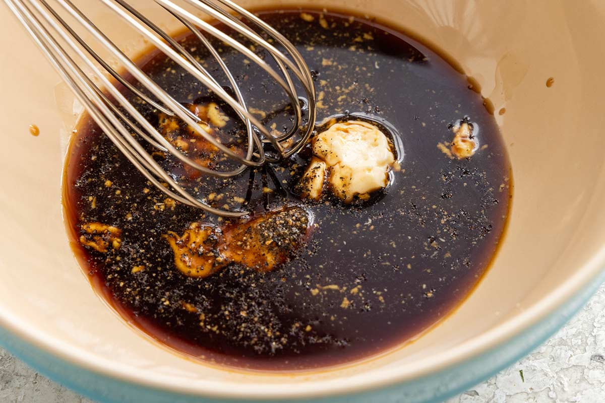Balsamic vinegar, Dijon mustard, mayonnaise, and spices in a bowl with a wire whisk.