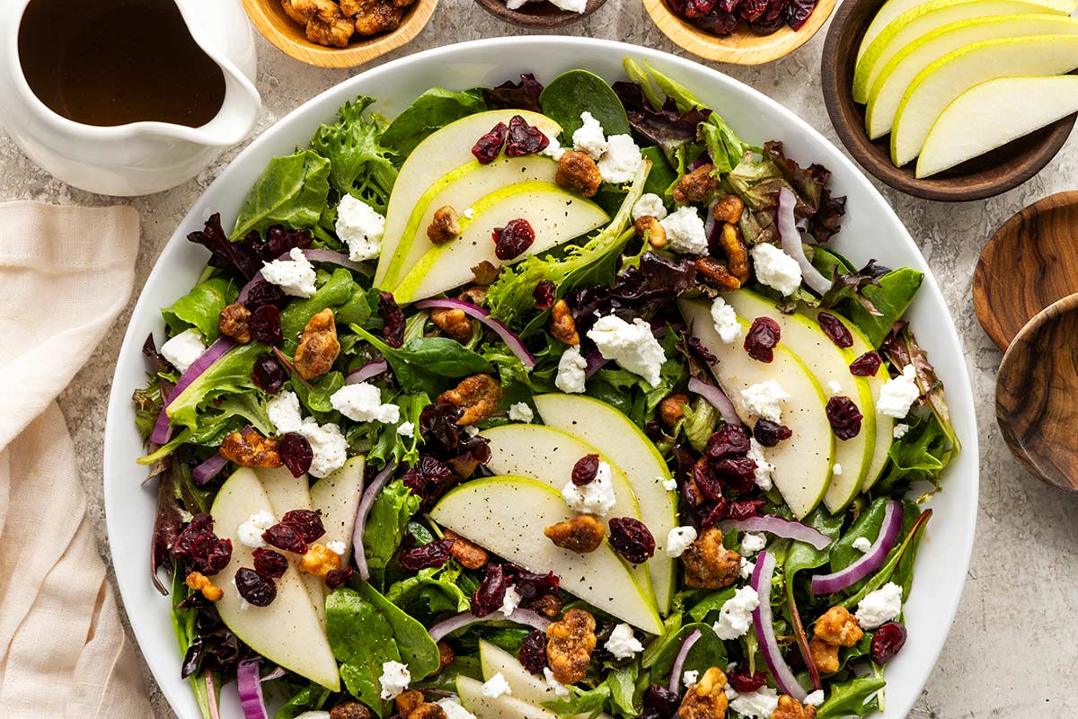 Top-down view of a bowl of pear salad with mixed greens, pear slices, goat cheese, dried cranberries, nuts, and red onion.