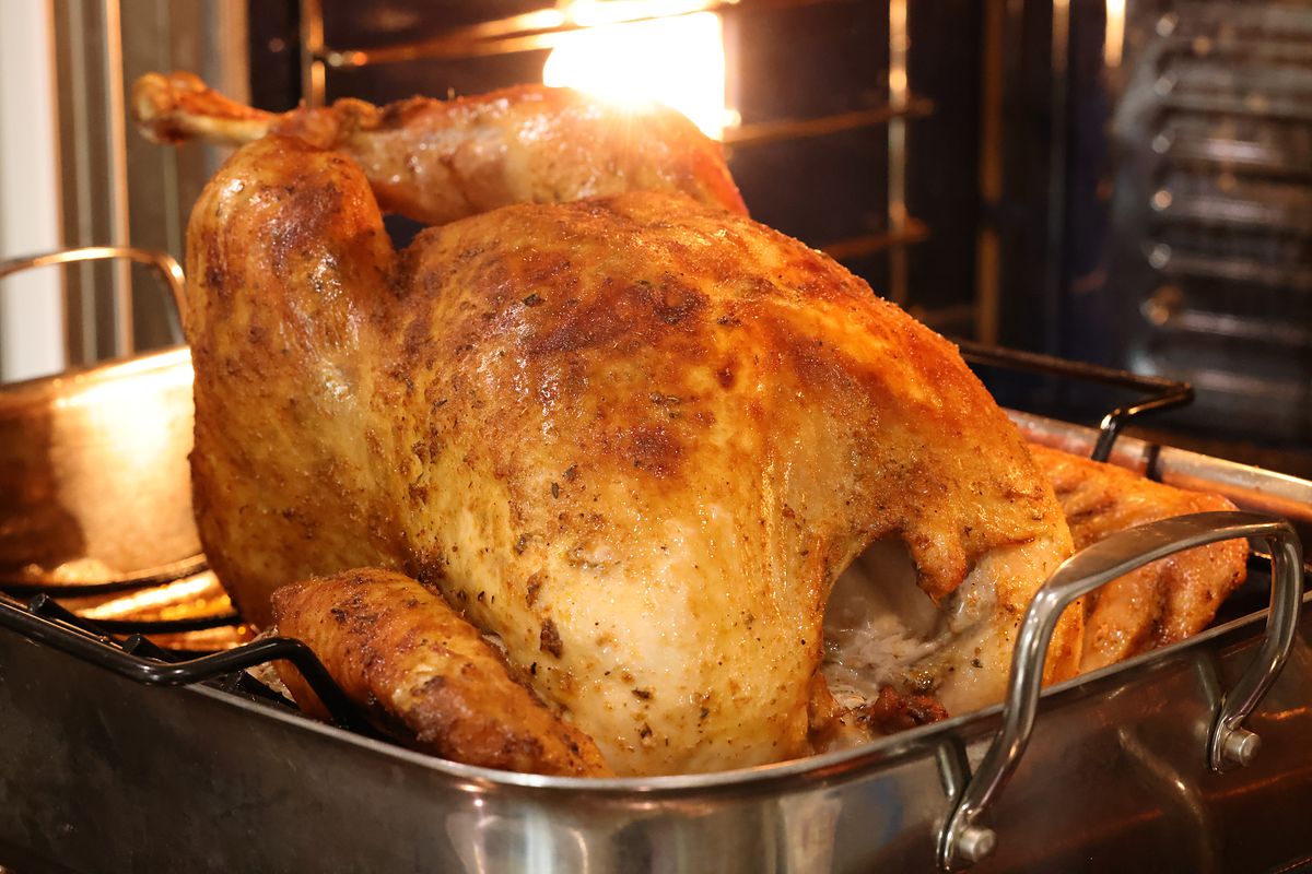 Seasoned turkey roasting and turning golden brown in a roasting pan inside the oven.